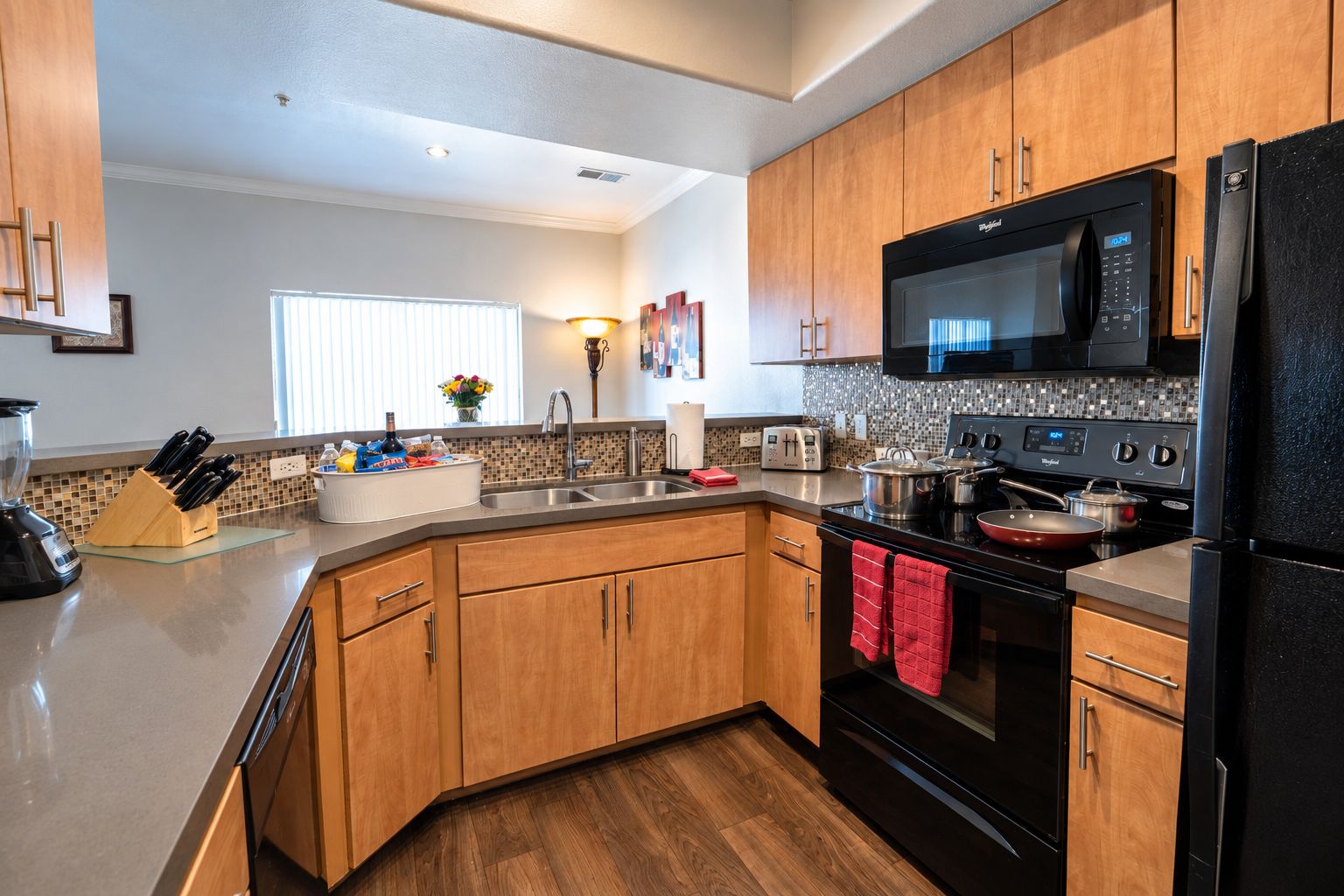 A modern kitchen with wooden cabinets, a black refrigerator, a microwave, a stove, and a sink.