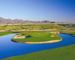 Um campo de golfe com lago, árvores e montanhas ao fundo.