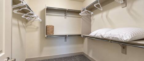 A small, compact hotel room with a bunk bed, a single bed with a pillow, a towel on the bed, and a wall-mounted shelf with a towel and a small item.