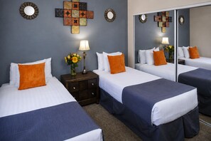 A hotel room with two beds, a nightstand with a lamp, a mirror, and wall art.