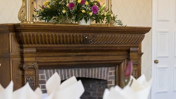 A dining table set with white napkins and glasses, a mirror above a fireplace, and a floral arrangement on the mantel.