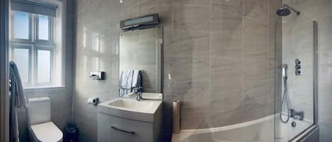 Un baño moderno con inodoro, lavamanos, espejo y ducha.