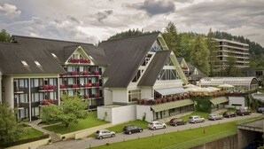A multi-story hotel with balconies, a parking area, and a view of a forested hill.