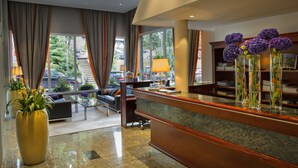 A hotel lobby with a reception desk, seating area, and large windows offering a view of the outside.