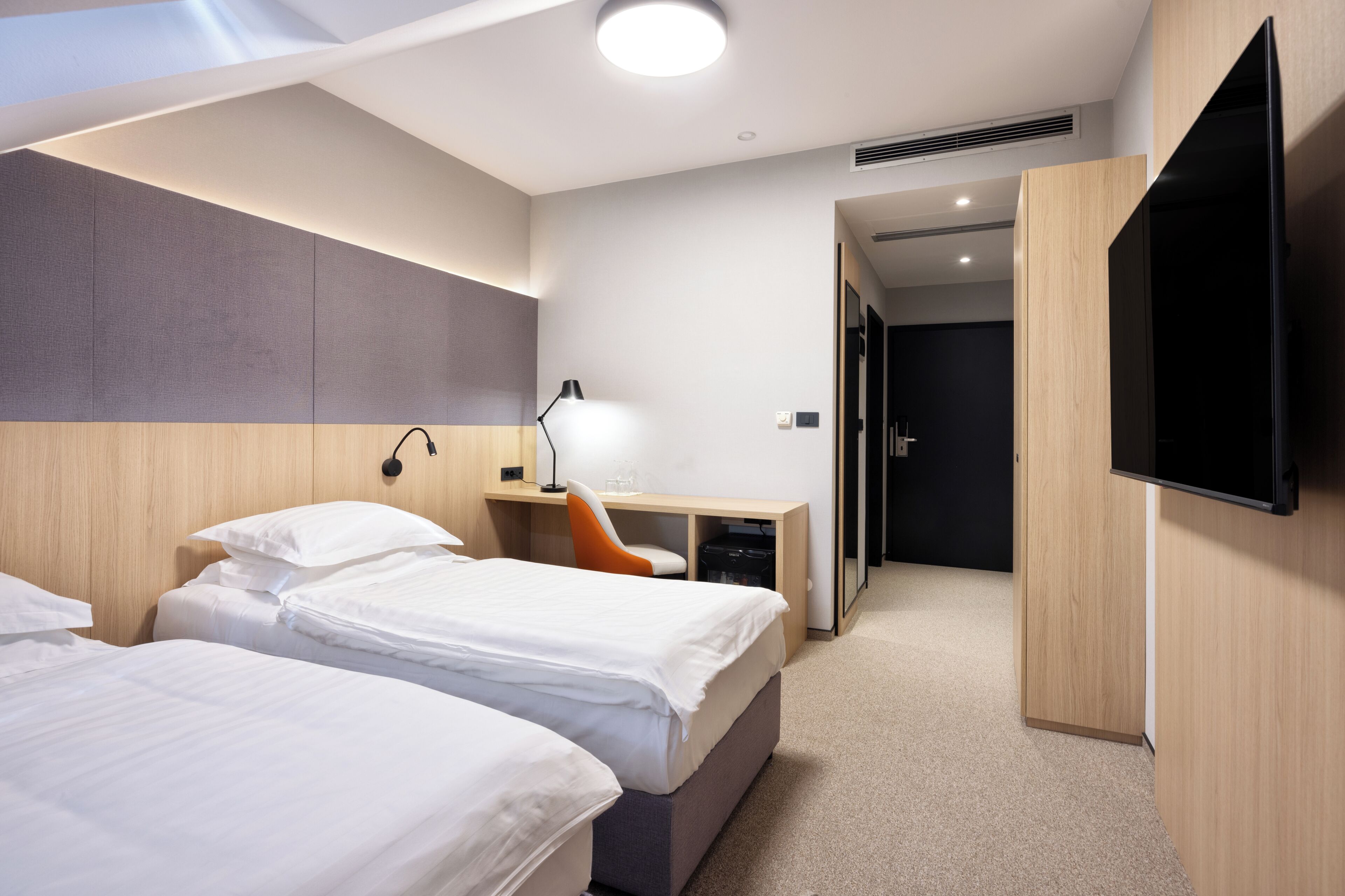 A hotel room with two beds, a desk with a chair, a TV, and a wardrobe.