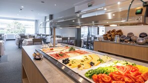 A buffet with various food items and a kitchen area in the background.