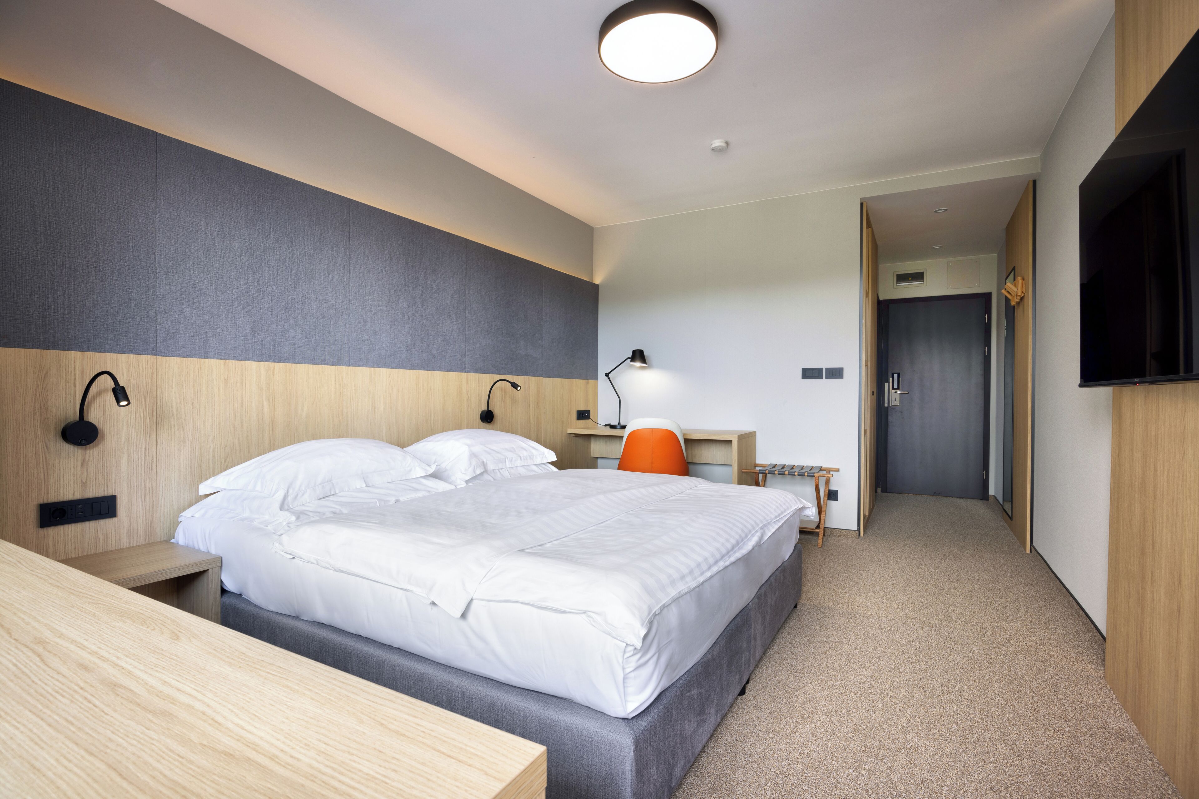 Una habitación de hotel moderna con una cama grande, un escritorio, una silla, un televisor y una puerta que da a otra habitación.