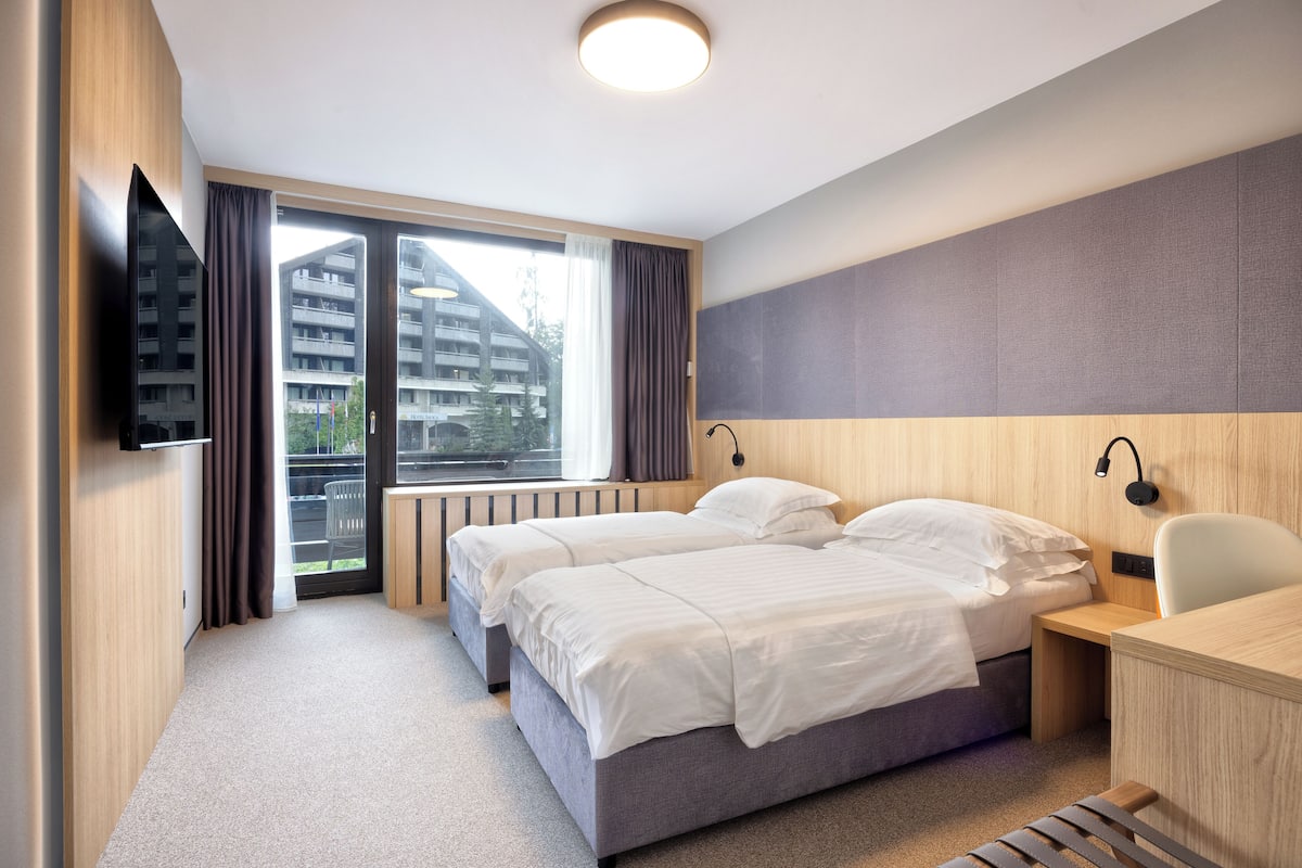 Quarto de hotel moderno com duas camas, uma escrivaninha e uma televisão.