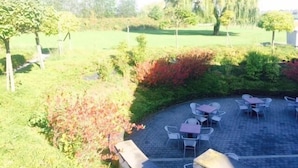 An outdoor seating area with tables and chairs, surrounded by greenery and trees.