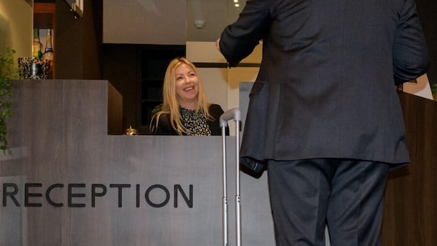 A reception desk with a sign that reads "RECEPTION" and a man standing beside a suitcase.