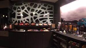 A bar area with a counter displaying various food items, a coffee machine, and a decorative car model.