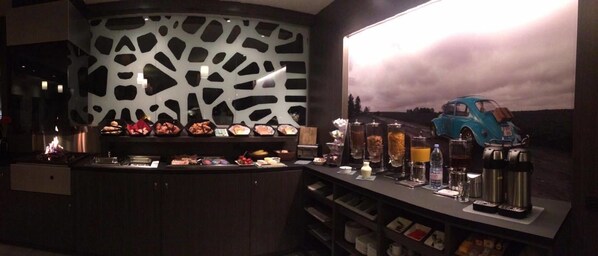 A bar area with a counter displaying various food items, a coffee machine, and a decorative car model.