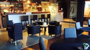 A bar area with a counter displaying various bottles, black upholstered chairs, and a modern interior design.