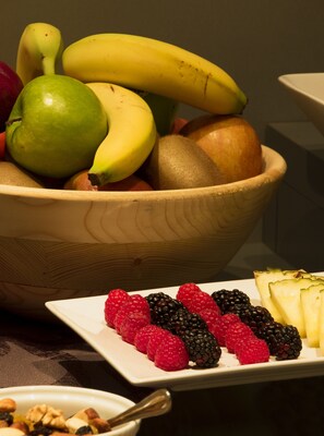 A wooden bowl filled with fruits including bananas, apples, and pears, and a plate with raspberries, blackberries, and pineapple slices.