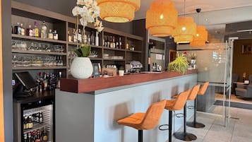 Zona de bar con estantes llenos de botellas de licor, una caja registradora y taburetes.