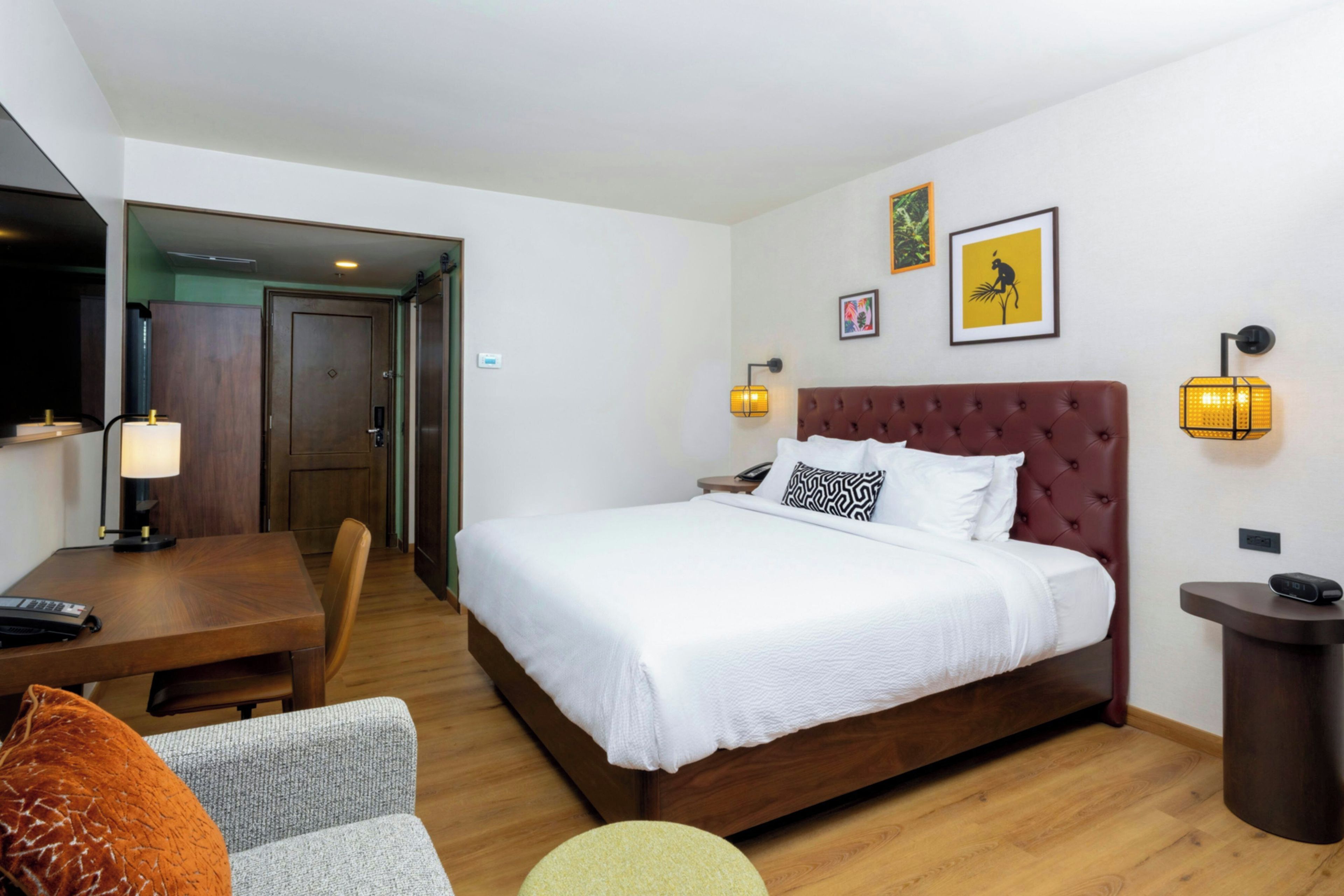 Una habitación de hotel con cama, mesita de noche, lámpara, silla y un escritorio con computadora.