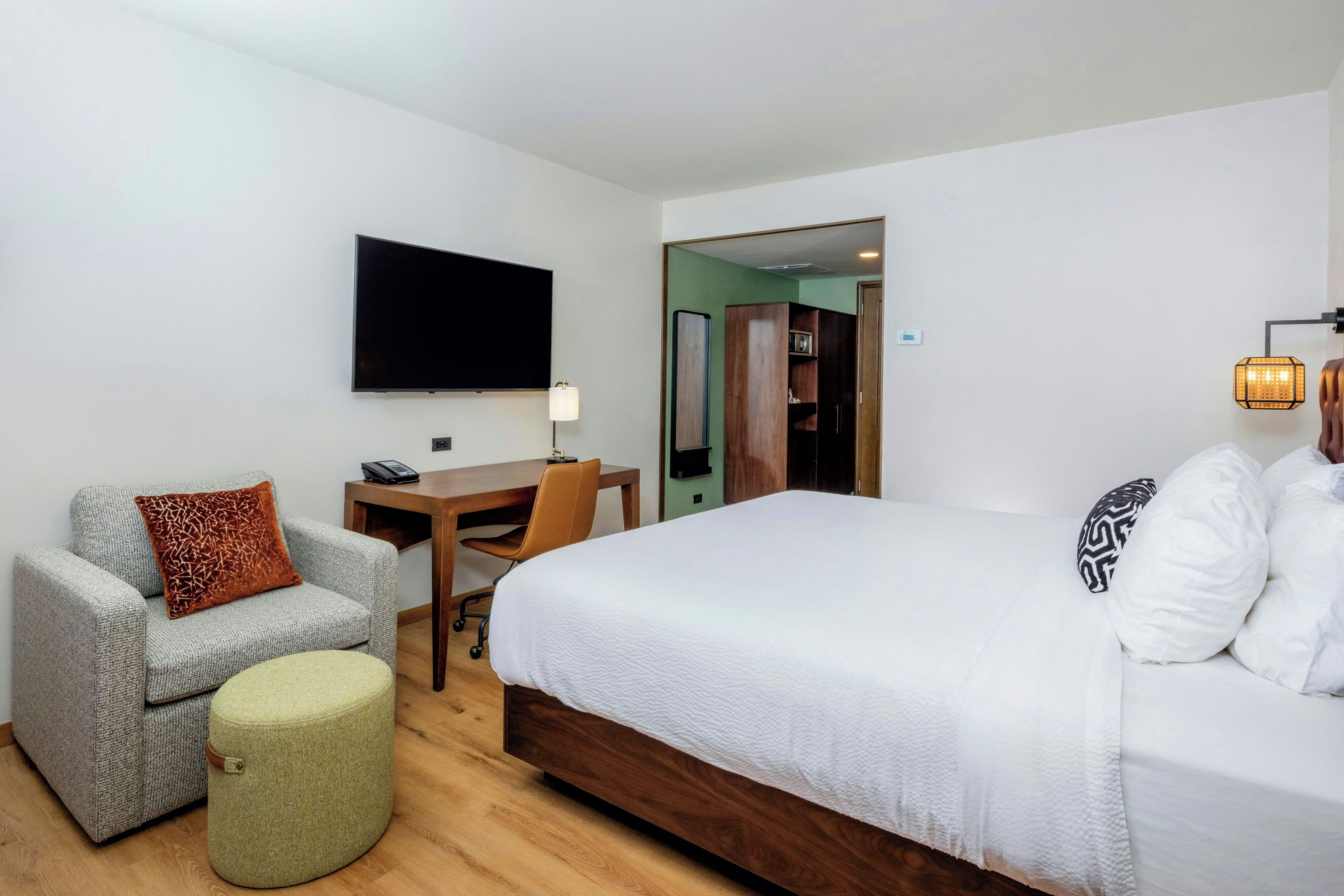 A hotel room with a bed, a desk, a chair, a television, and a lamp.
