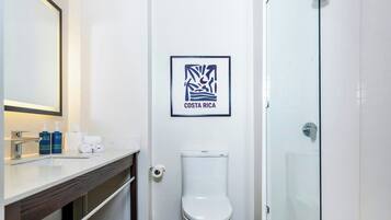 A bathroom with a white toilet, a framed picture of Costa Rica, and a glass shower enclosure.