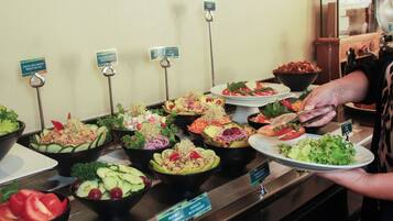 A buffet with various salads and a person serving food.