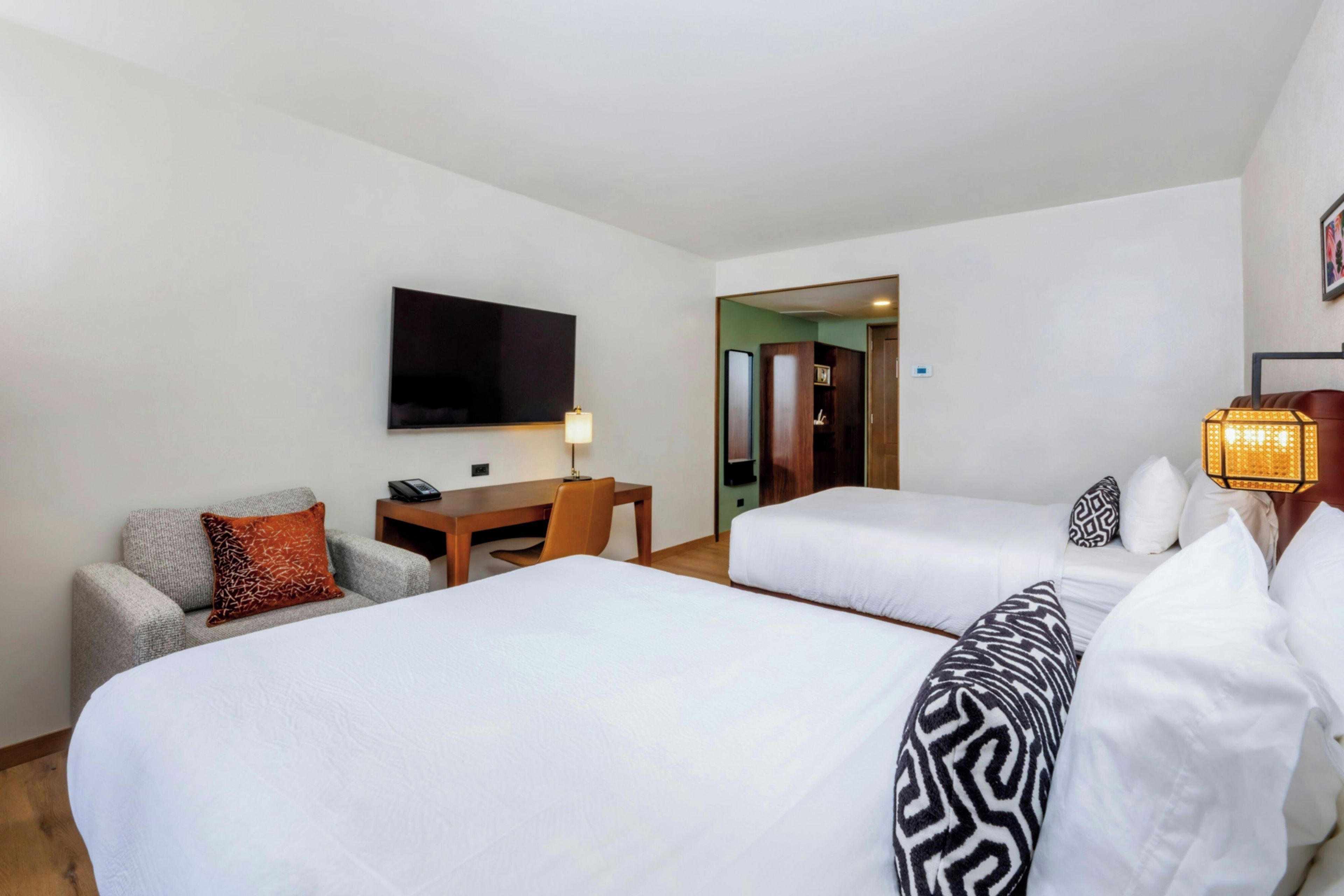 Ett hotellrum med två sängar, ett skrivbord, en stol, en TV och en lampa.