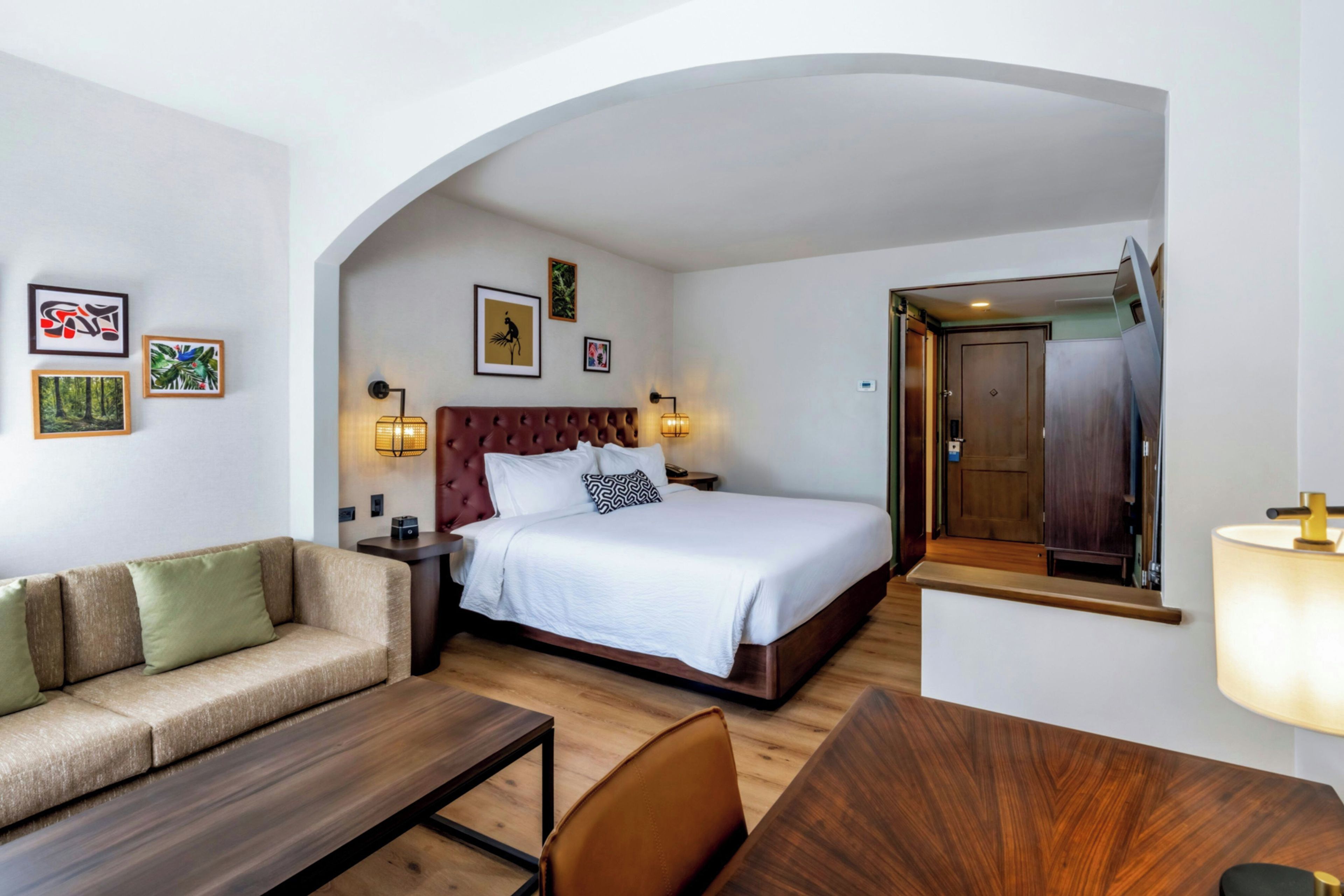 A hotel room with a bed, a sofa, a desk, and a mirror.