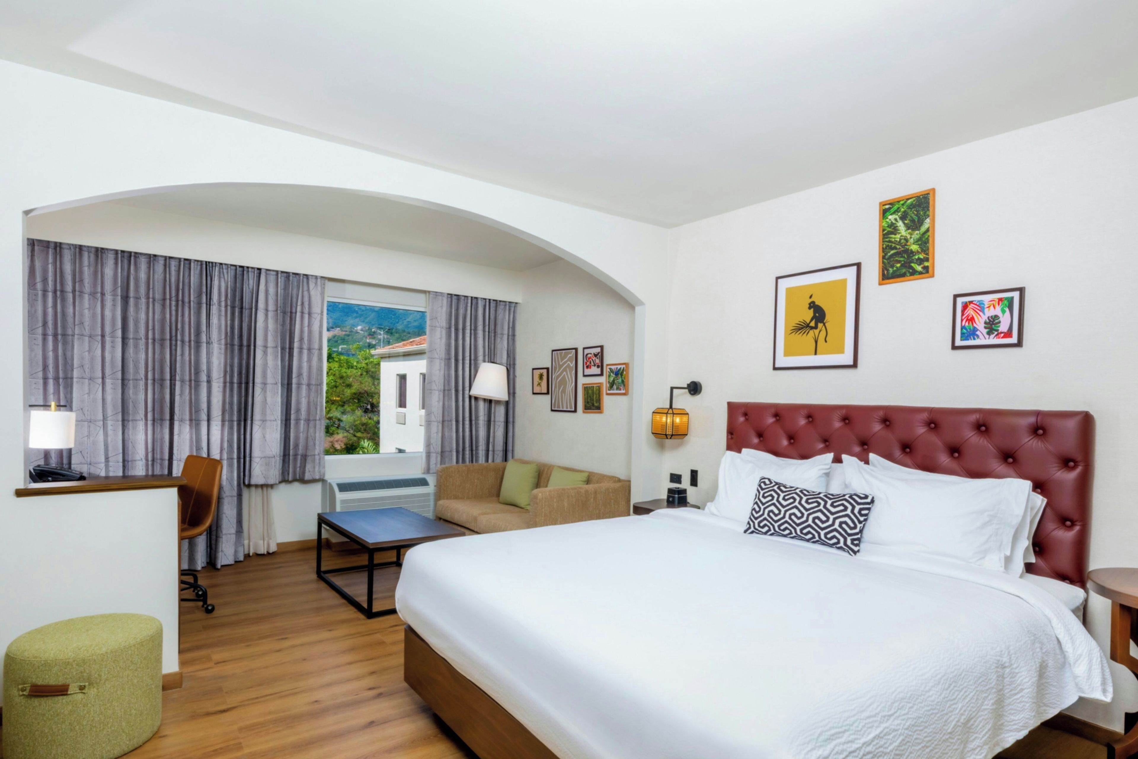 Habitación de hotel con cama, escritorio, silla, sofá y vistas al exterior.