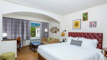 Habitación de hotel con cama, escritorio, silla, sofá y vistas al exterior.