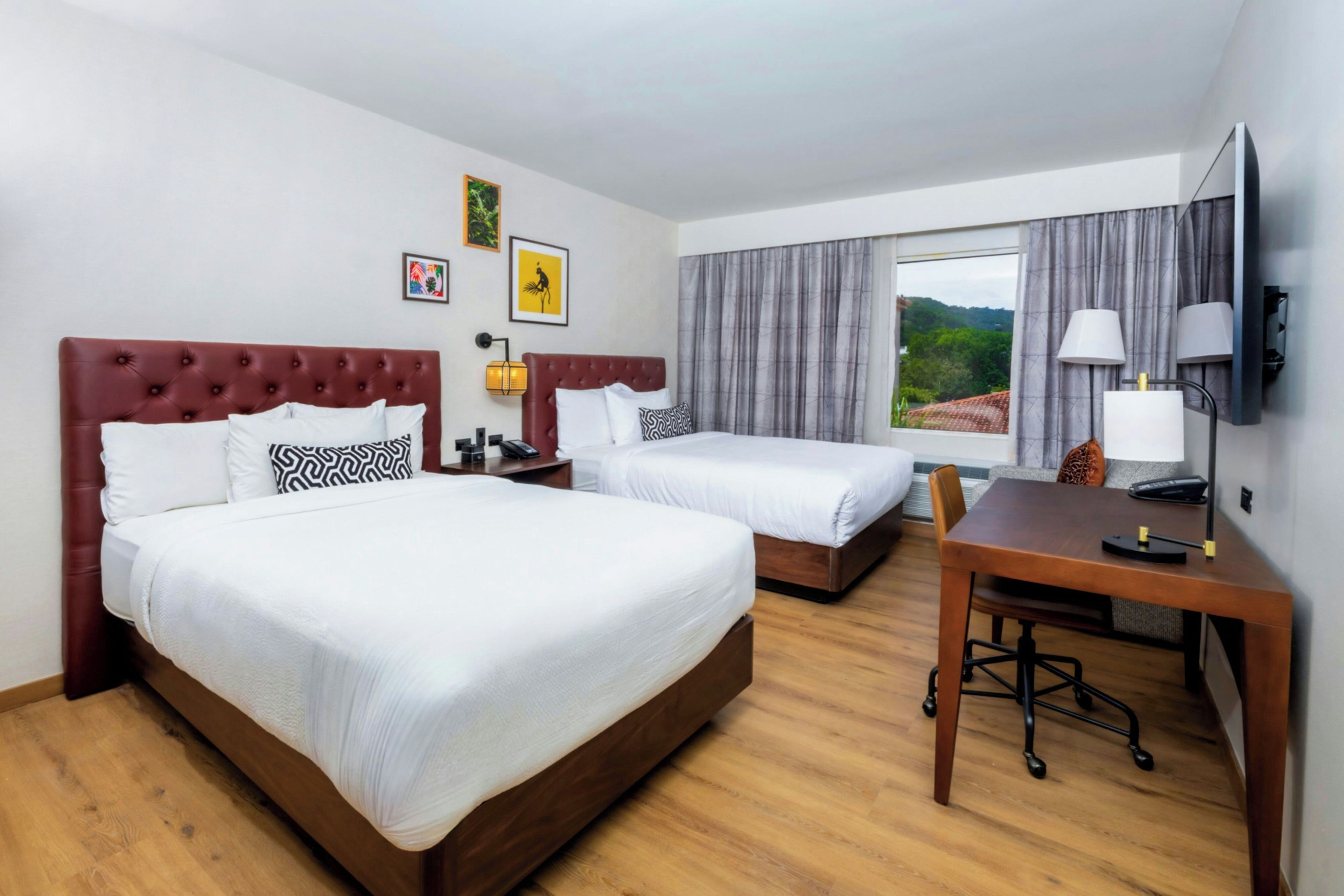 A hotel room with two beds, a desk, a chair, a TV, and a window with curtains.