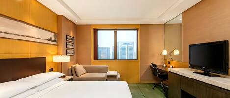 Habitación de hotel con cama, escritorio con televisor, silla, mesita y ventana con vista a la ciudad.