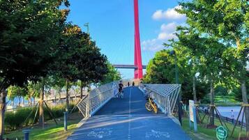 A pedestrian bridge with a red structure in the background, surrounded by trees and a body of water.