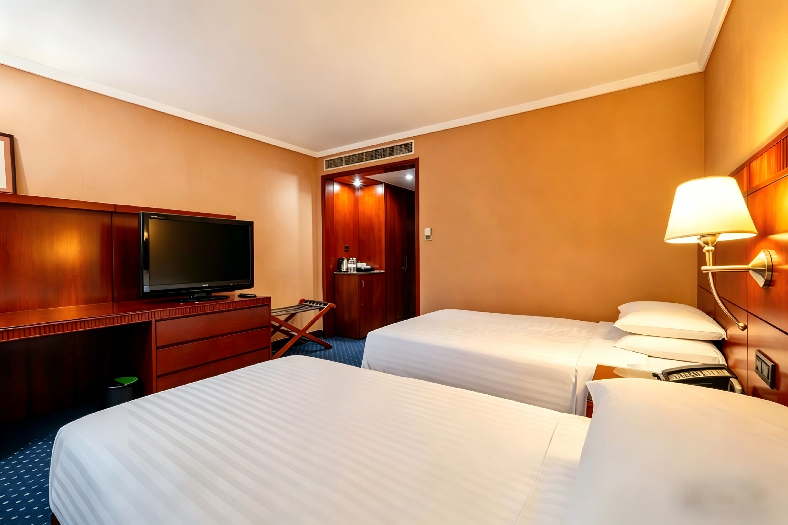 A hotel room with two beds, a TV, a desk, a lamp, and a wardrobe.