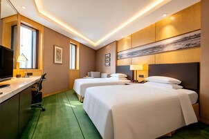 A hotel room with two beds, a desk, a TV, and a large window.