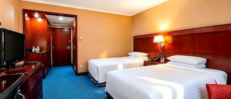 A hotel room with two beds, a TV, a desk with a computer, and a red chair.