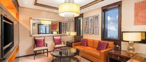 A modern hotel room with a large flat-screen TV, a glass coffee table, a sofa, and a chandelier.