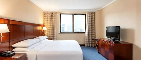 A hotel room with a bed, a television, a desk with a telephone, and a window with curtains.