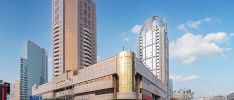 A modern building with a curved facade and a prominent cylindrical section, surrounded by high-rise buildings.