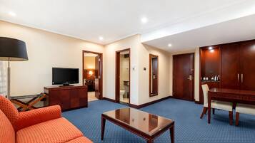 Quarto de hotel com sofá, televisão, mesa de jantar e armário.