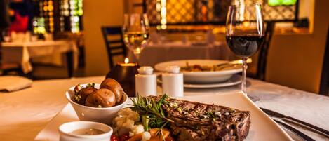 A dining table with a steak, vegetables, and a glass of wine.