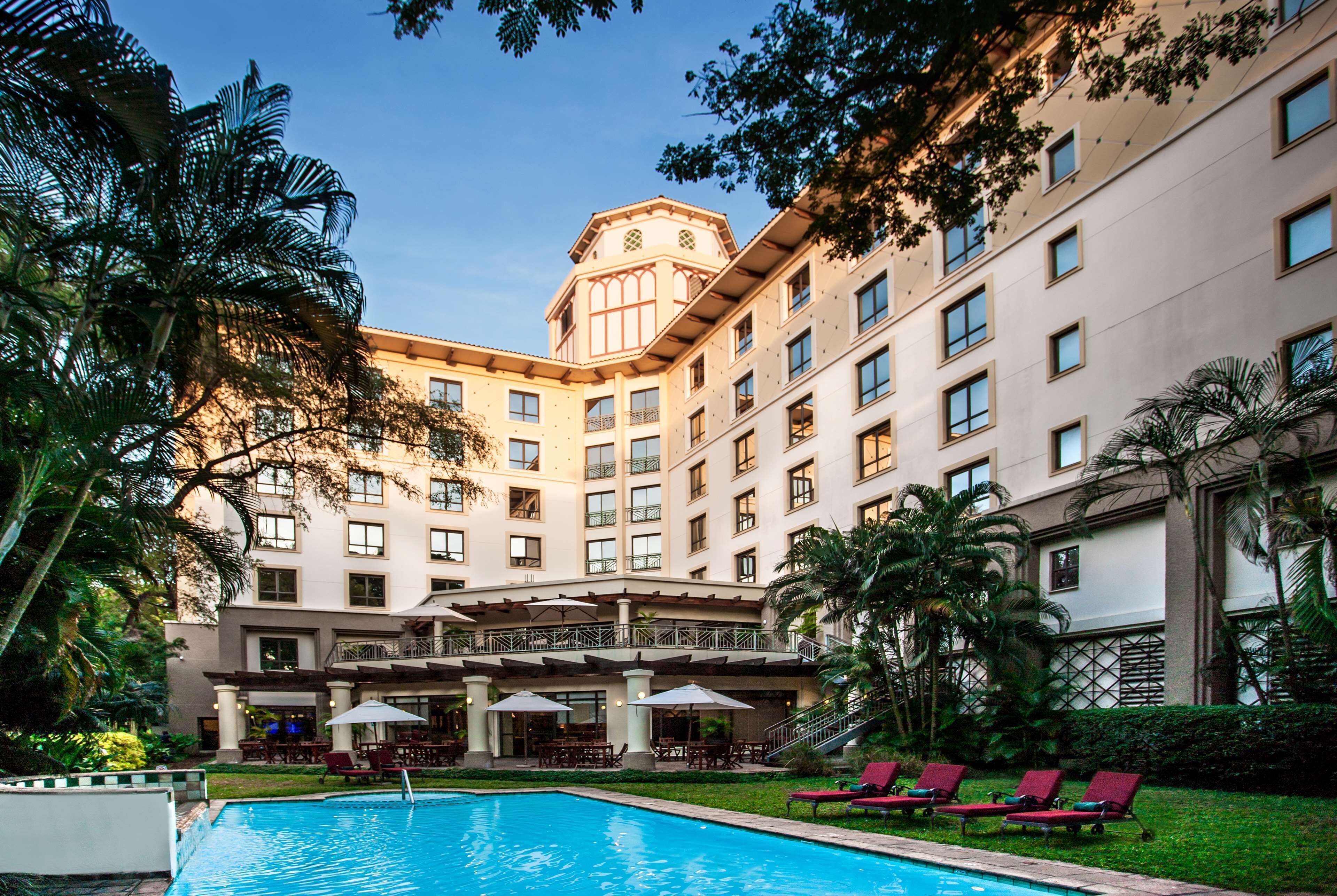 A hotel with a swimming pool, outdoor seating, and palm trees.