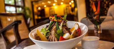 A bowl of salad with grilled chicken, vegetables, and a small bowl of dressing on a white plate.