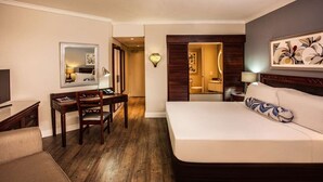 Een hotelkamer met een bed, een bureau, een stoel, een televisie en een badkamer die door een open deur zichtbaar is.