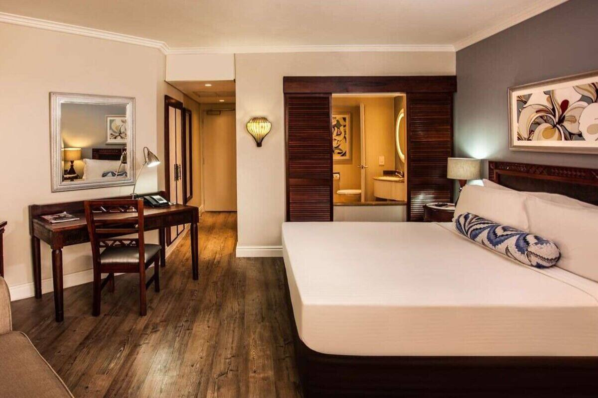 A hotel room with a bed, a desk, a chair, a TV, and a bathroom visible through an open door.