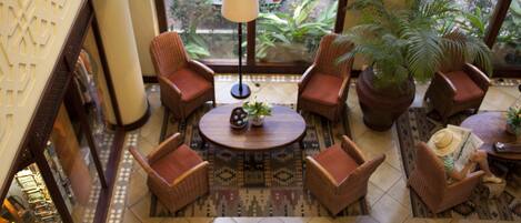 A lobby with a round table, four wicker chairs, a large potted plant, and a patterned rug.