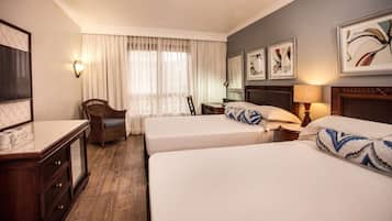 A hotel room with two beds, a desk, a chair, a lamp, and artwork on the walls.