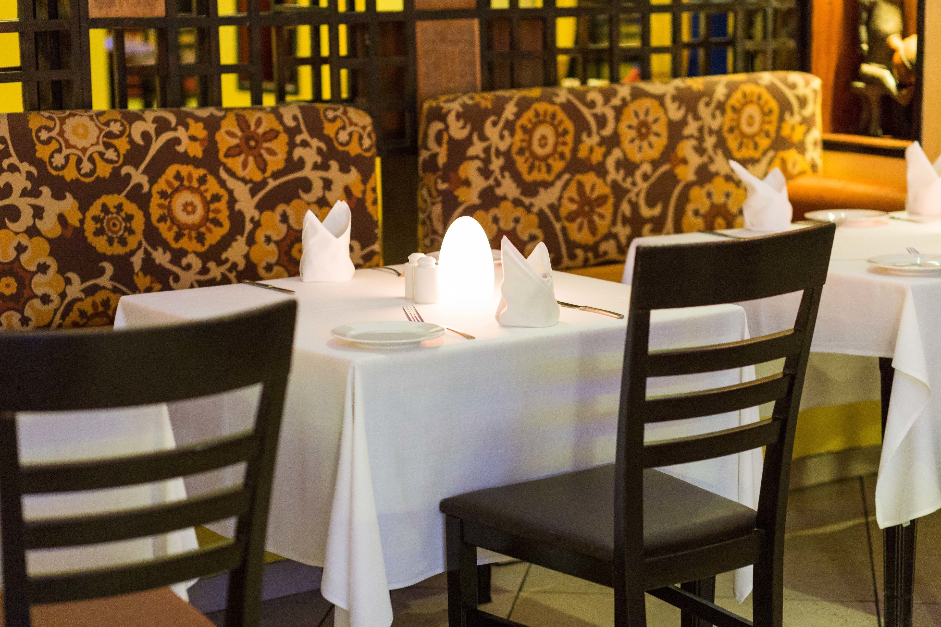 Un ristorante con tovaglie bianche, sedie nere e cuscini decorati sui posti a sedere.