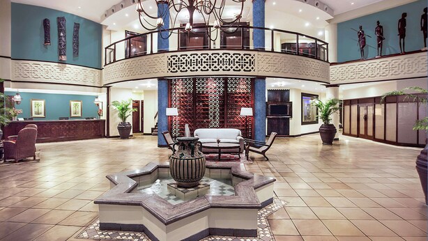 Een ruime lobby met een centrale fontein, zitgedeeltes en een decoratieve wand met een geometrisch patroon.