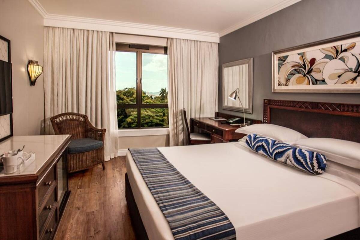 Een hotelkamer met een bed, een bureau, een stoel, een raam met gordijnen en een schilderij aan de muur.