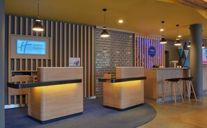 A hotel reception area with wooden reception desks, a digital display, and a wall with a geometric pattern.