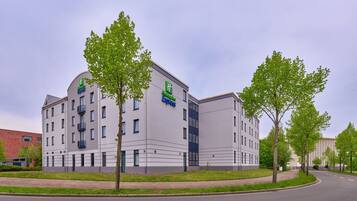 Um edifício moderno de hotel com telhado plano, várias janelas e uma placa verde e azul bem visível indicando ser um Holiday Inn Express.