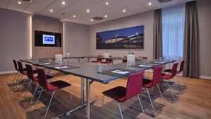 A conference room with a long table, red chairs, a flat-screen TV, and a painting on the wall. - Holiday Inn Express Dortmund by IHG (Dortmund)